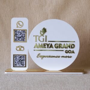 An elegant social media QR code stand made of white acrylic with shiny gold details, customized for the "TGI Ameya Grand Goa" hotel.