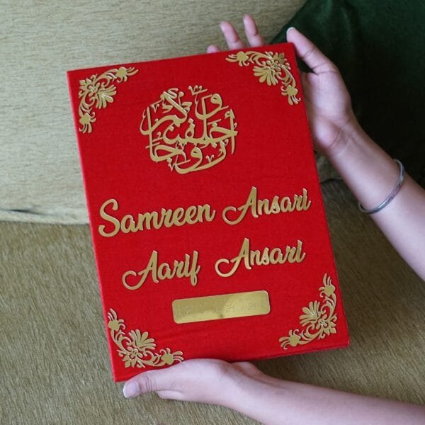 A person's hands holding a large, luxurious red and gold custom Nikah Nama booklet, showcasing its premium quality and size.