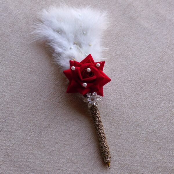 “Close-up of a decorative Nikah signing pen featuring a glittery lace-wrapped barrel, a red artificial rose with pearl-studded floral accents, and white feather plumes.”