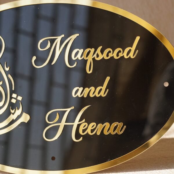 Black oval acrylic nameplate with gold Arabic calligraphy, featuring a small dangling gold heart plate embossed with the child’s name—a personalized, elegant keepsake for your home.