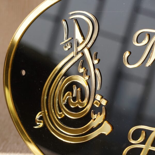 Black oval acrylic nameplate with gold Arabic calligraphy, featuring a small dangling gold heart plate embossed with the child’s name—a personalized, elegant keepsake for your home.