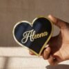 Black oval acrylic nameplate with gold Arabic calligraphy, featuring a small dangling gold heart plate embossed with the child’s name—a personalized, elegant keepsake for your home.