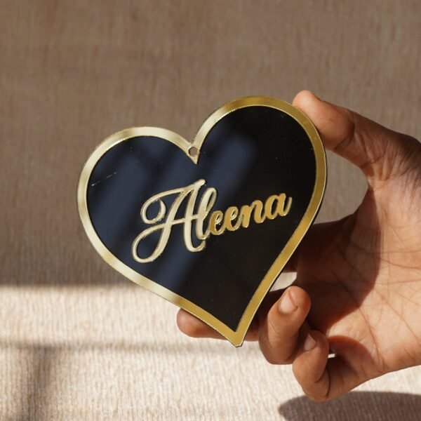 Black oval acrylic nameplate with gold Arabic calligraphy, featuring a small dangling gold heart plate embossed with the child’s name—a personalized, elegant keepsake for your home.