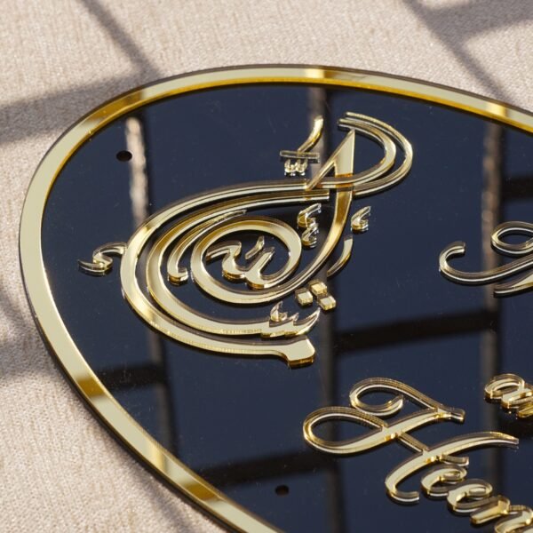 Black oval acrylic nameplate with gold Arabic calligraphy, featuring a small dangling gold heart plate embossed with the child’s name—a personalized, elegant keepsake for your home.