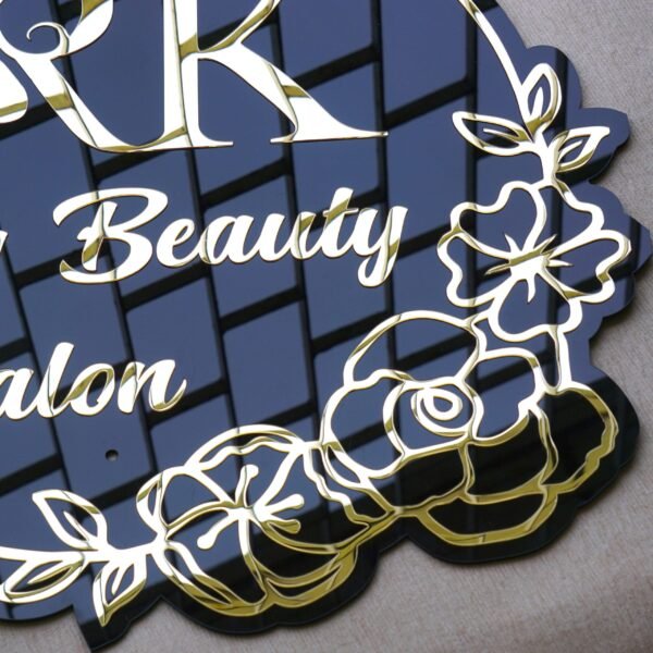 Detailed close-up of the intricate floral border and gold lettering on the black acrylic beauty salon sign.