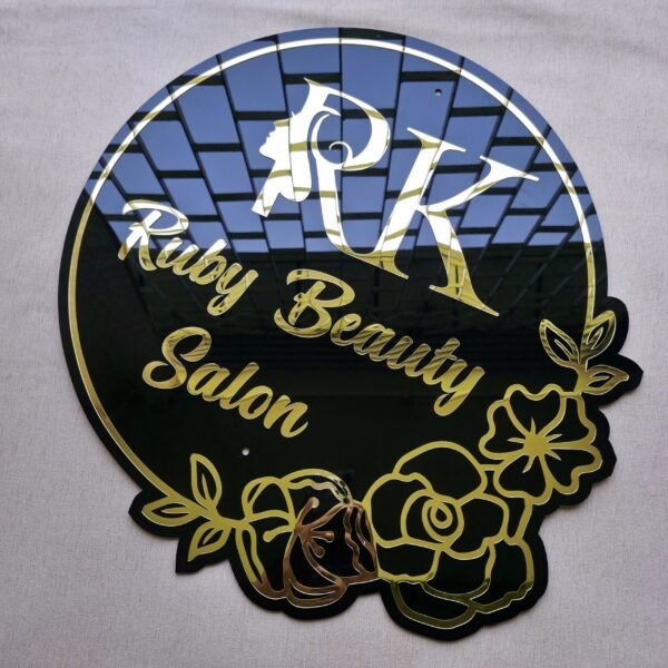 Angled view of the black and gold salon sign showing the mirror reflection on the 3D gold letters and pre-drilled mounting holes.