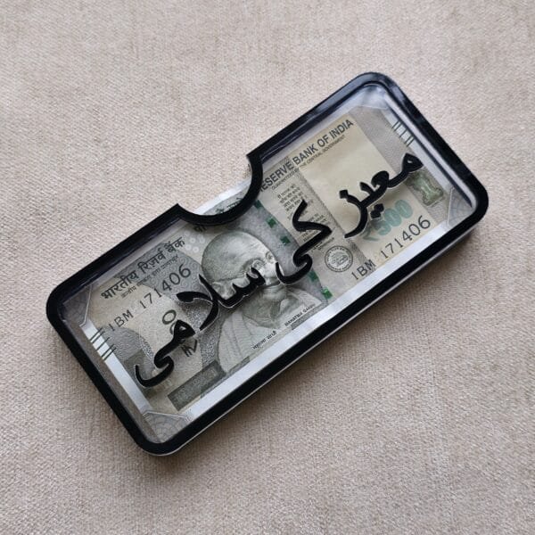 20250613_144628 Angled view of a personalized acrylic money holder with 'Moez Ki Salami' in Urdu calligraphy, highlighting the raised 3D lettering.