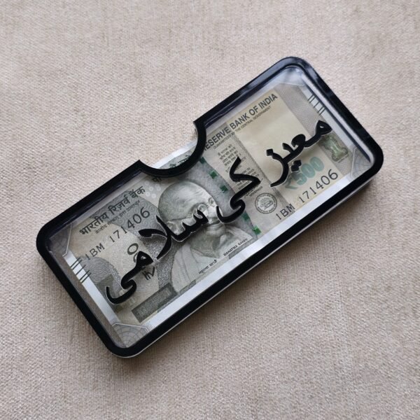 Angled view of a personalized acrylic money holder with 'Moez Ki Salami' in Urdu calligraphy, highlighting the raised 3D lettering.