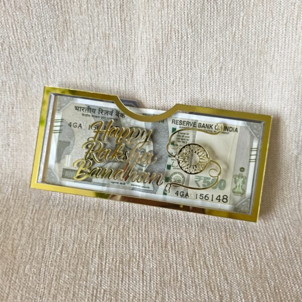 An elegant gold acrylic shagun envelope for Raksha Bandhan, shown at an angle to display its glossy finish and the 'Happy Raksha Bandhan' design.