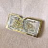 A stylish Raksha Bandhan money gift holder made of clear acrylic with shiny gold accents, with a 500 rupee note visible inside.