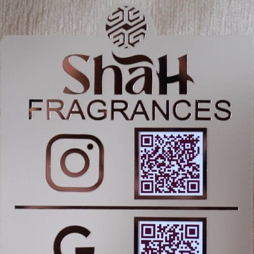 Close-up of the custom logo and 'Shah Fragrances' brand name on a rose gold acrylic QR display, with the Instagram logo and QR code below.