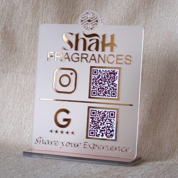 Angled view of a custom rose gold acrylic QR code stand for 'Shah Fragrances' on its display base, showing its 3D profile.
