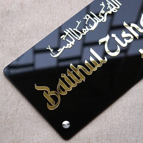 Angled view showing the 3D effect of the golden 'Baithul Zishaan' lettering on the glossy black acrylic nameplate.