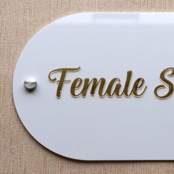 Close-up of the raised gold acrylic lettering on the 'Female Section' shop sign, showing the elegant script.