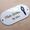 Angled view of the 'Male Section' shop sign, showing the glossy finish of the white acrylic and raised gold letters.