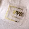 Front view of a custom gold and clear acrylic business sign with the text "VVS Moments..." against a light-colored fabric background.