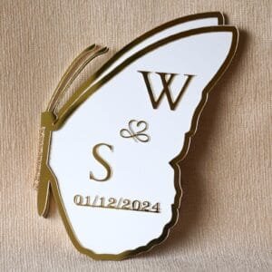 A folded white and gold butterfly nikah board showing the wing with custom initials 'W & S' and the date '01/12/2024' in golden acrylic.