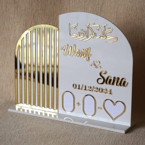 A clear, front-facing view of the personalised Nikah thumb board for 'Wasif & Sana', highlighting the shiny gold acrylic lettering and date against the white plaque.