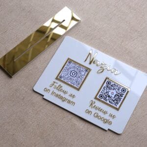 White acrylic business QR code sign with gold lettering shown lying flat next to its detachable gold mirror acrylic base, highlighting its portable design.