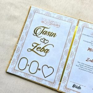 Close-up of the inside left page of the Nikah Nama, showing the names 'Tasin' and 'Zeba' in beautiful gold foil script.