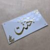 Top-down view of a glossy white acrylic nameplate, with the name 'Jannat' and corner accents in brilliant, reflective gold lettering.