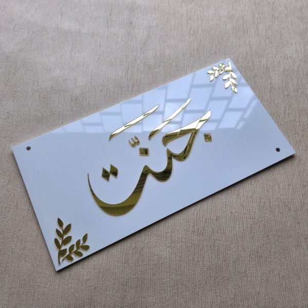 Top-down view of a glossy white acrylic nameplate, with the name 'Jannat' and corner accents in brilliant, reflective gold lettering.