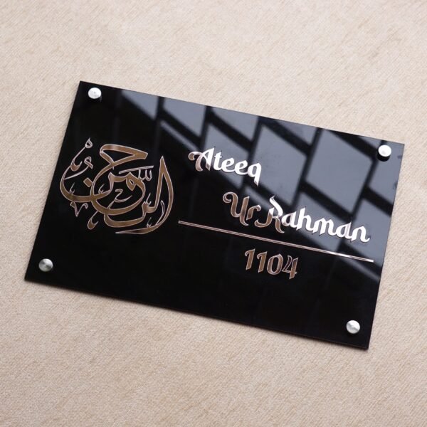 An angled view of the glossy black Islamic name plate, showing reflections on its surface and the shine of the rose gold lettering.