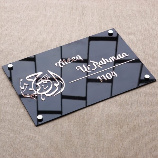 The black acrylic door sign with rose gold 'Al-Rahman' calligraphy viewed from a top-down angle, highlighting its slim profile.
