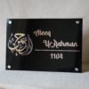 Close-up of a modern acrylic nameplate featuring elegant Arabic calligraphy and personalized details, mounted with four silver studs.