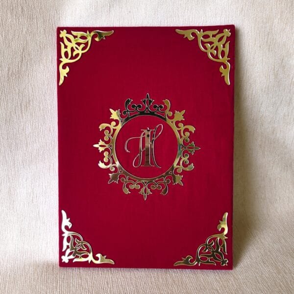 nn2 Closed red velvet-textured Nikah Nama booklet with a custom gold acrylic monogram 'IH' in an ornate central design.