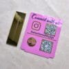 The two separate pieces of the QR code stand laid flat: the pink engraved plaque and the reflective gold base, showing the product before assembly.