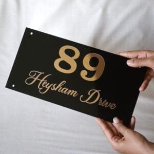 np1 A person holding a modern black acrylic and rose gold house name plate for "89 Heysham Drive" to show its size and quality.