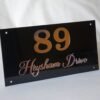 np4 Angled view of an elegant black acrylic nameplate for "89 Heysham Drive," highlighting the reflective quality of the rose gold custom text.