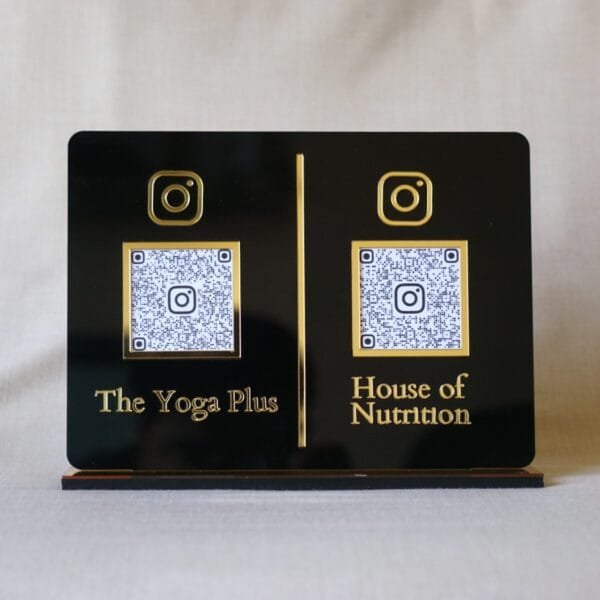 Front-facing view of a custom dual QR code display stand in black and gold acrylic, featuring Instagram links for 'The Yoga Plus' and 'House of Nutrition'.
