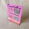 Three-quarter perspective of the custom pink and gold QR code stand for a boutique, showing the clear reflection on the gold accents.
