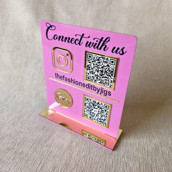 Three-quarter perspective of the custom pink and gold QR code stand for a boutique, showing the clear reflection on the gold accents.