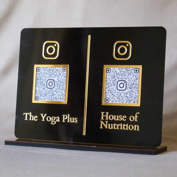 A professional black and gold acrylic QR code plaque standing upright on its base, showing two scannable codes for social media branding.