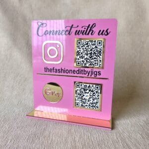 Angled side view of the pink acrylic social media and payment QR code display stand, highlighting the glossy gold base and 3D logos.