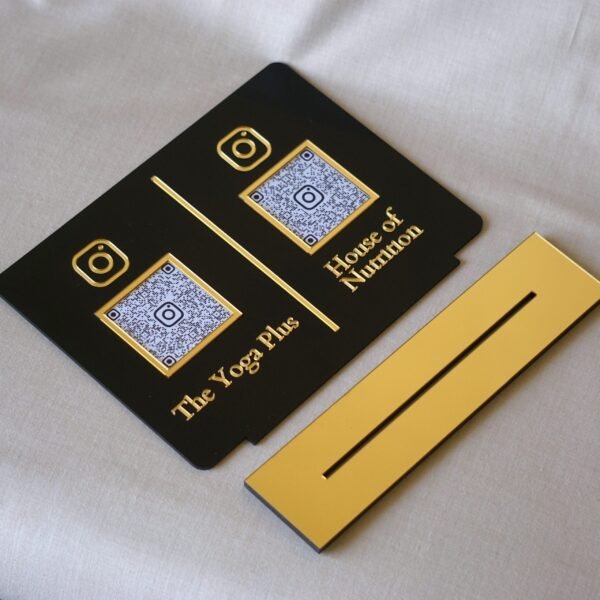 The black and gold dual QR code plaque shown separated from its reflective gold acrylic base, highlighting its removable and versatile design.