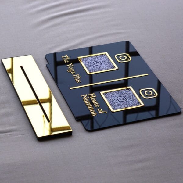An angled view of the premium dual QR code sign and its gold stand, showcasing the glossy acrylic finish and raised gold text.