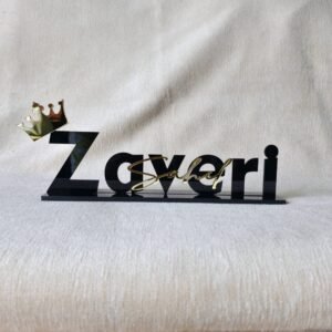 Custom black acrylic desk nameplate for 'Sahel Zaveri' with a gold crown, shown from the front on a beige textured background.
