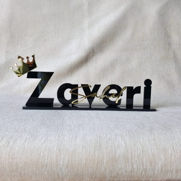 Custom black acrylic desk nameplate for 'Sahel Zaveri' with a gold crown, shown from the front on a beige textured background.