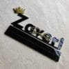 Top-down angled view of the custom acrylic desk sign with gold lettering and a crown on a textured surface.