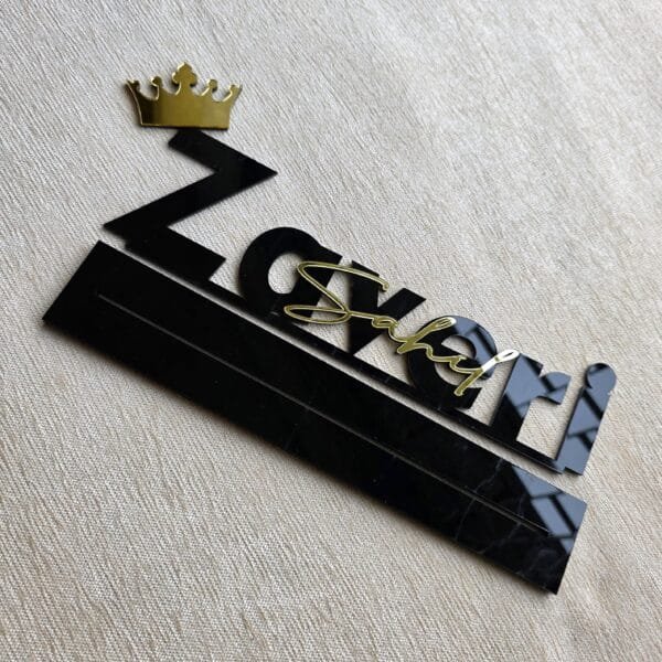 Top-down angled view of the custom acrylic desk sign with gold lettering and a crown on a textured surface.