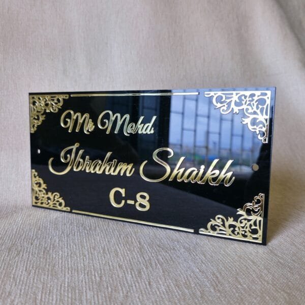 Angled view of the black and gold acrylic nameplate showing the glossy, reflective surface and 3D embossed text.