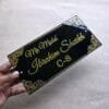 A hand holding the black and gold acrylic nameplate to show its size and premium finish.