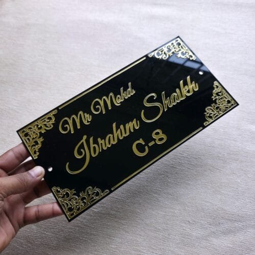 A hand holding the black and gold acrylic nameplate to show its size and premium finish.