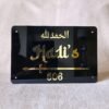 A straight-on view of a personalized Islamic nameplate in black acrylic, featuring a decorative sword and 'Alhamdulillah' in gold.