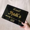 Hand holding a custom black and gold Islamic acrylic nameplate to show its size and glossy finish.