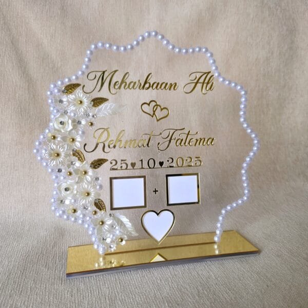 Front view of a personalized acrylic Nikah thumb board with a pearl frame, gold lettering, and white floral details, standing upright on its gold base.